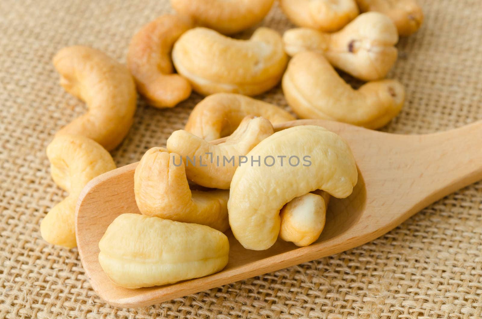 cashew nuts with salt and wooden spoon on sack background.