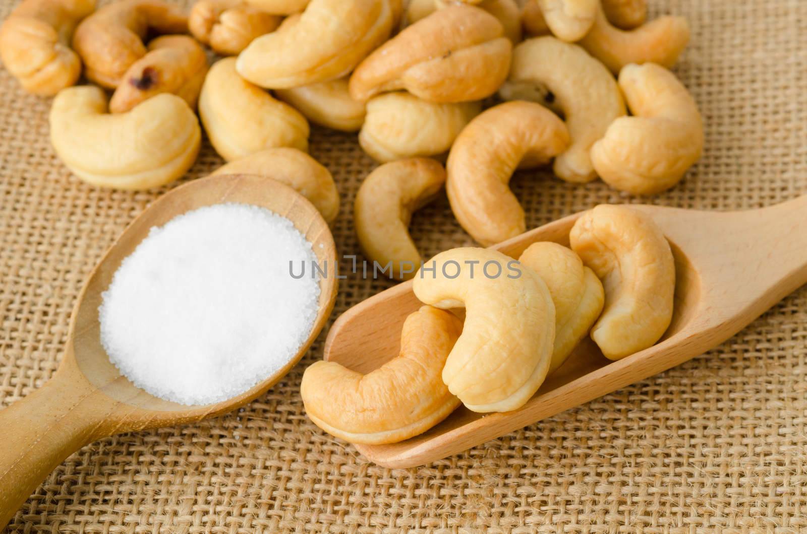 Roasted cashews and salt in wooden spoon on natural sack background