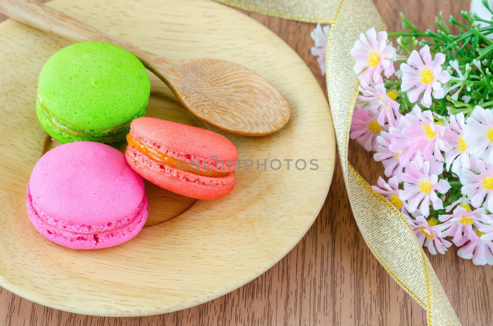 Colorful macaroons, delicious French pastries and flower on wooden background.