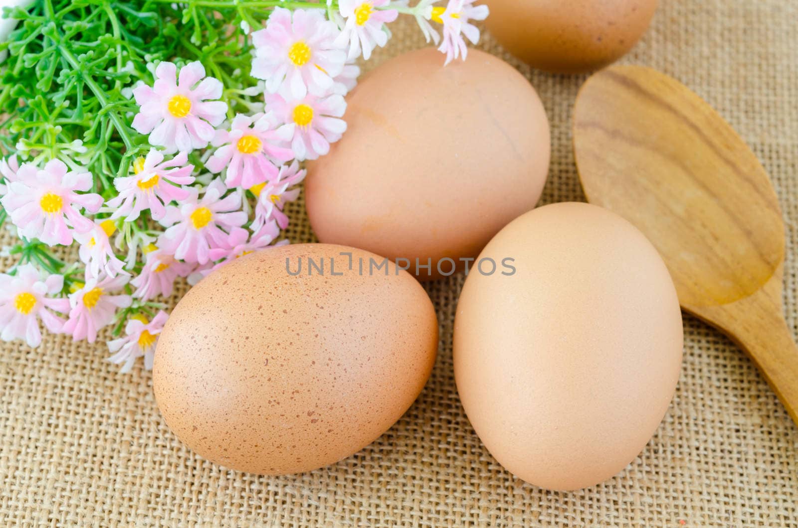 Eggs and wooden spoon with flower on sack background.