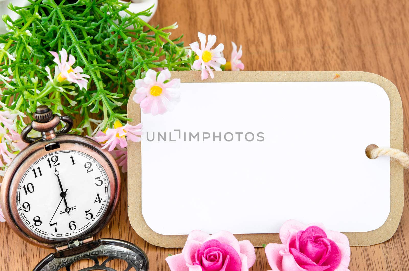 Blank greeting card and pocket watch with flower on wooden background.