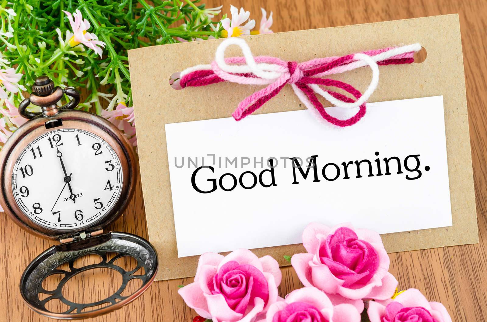Good morning in greeting card and pocket watch on wooden background.