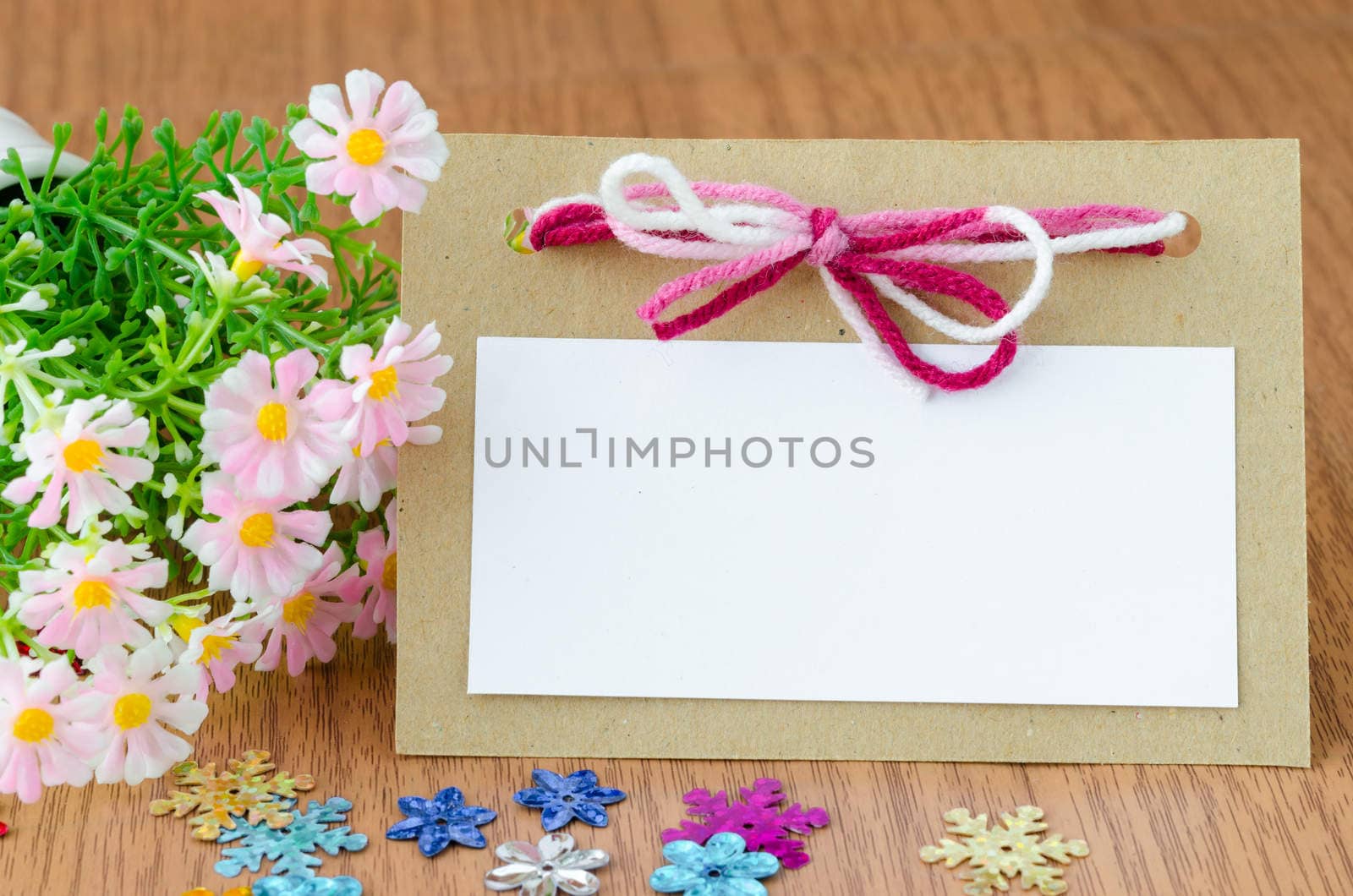 Blank greeting card with pink ribbon and flower on wooden background.