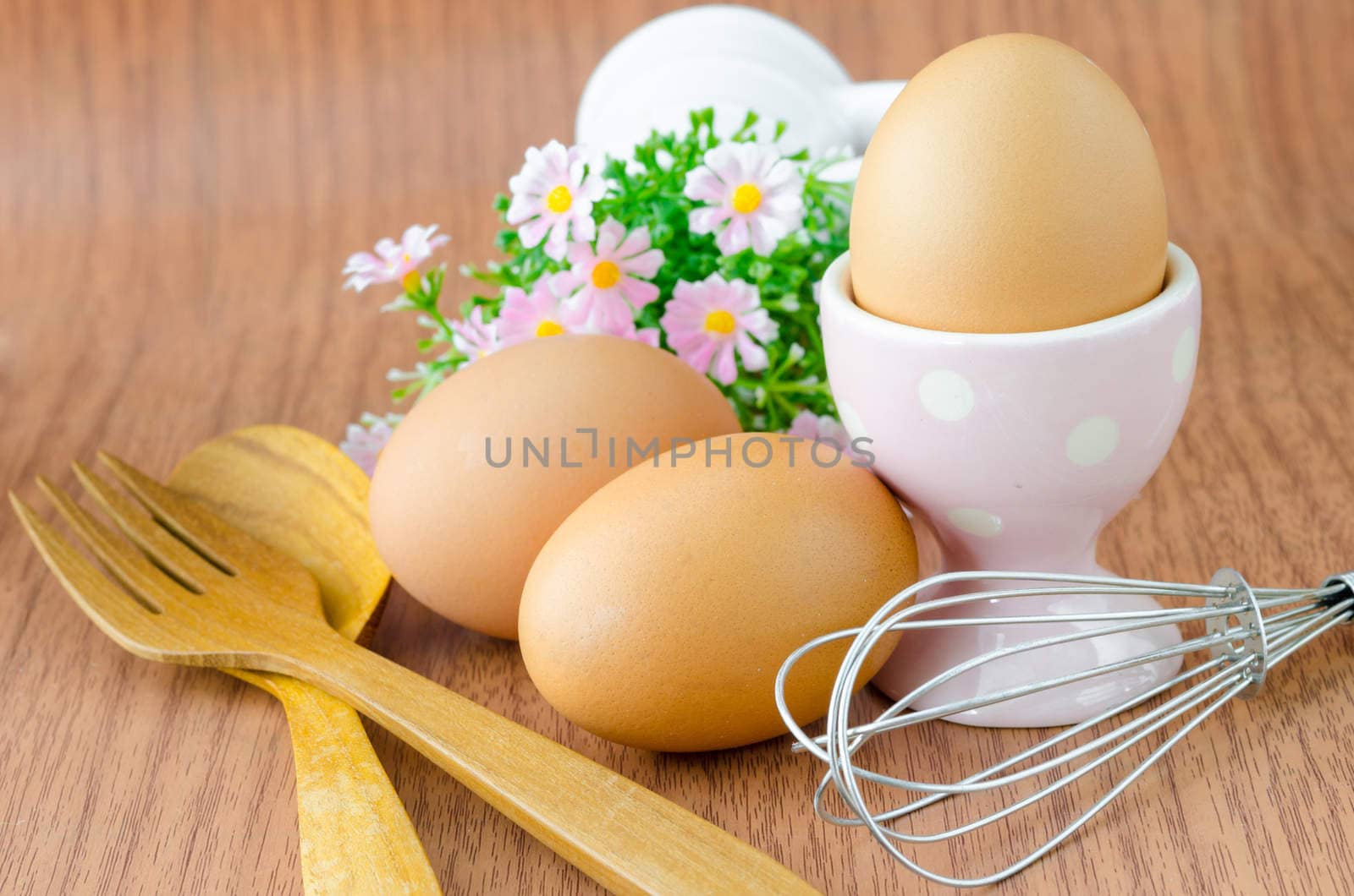 Eggs in bowl and wooden spoon with flower on wooden background.