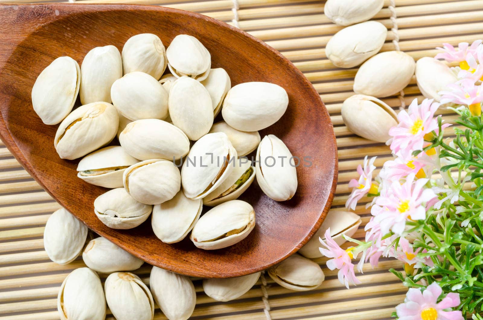 Roasted pistachios in wooden spoon and milk in glass with flower on mat wooden background.