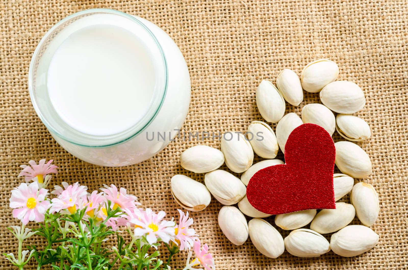 Pistachio nuts and milk in glass with flower on sack background.