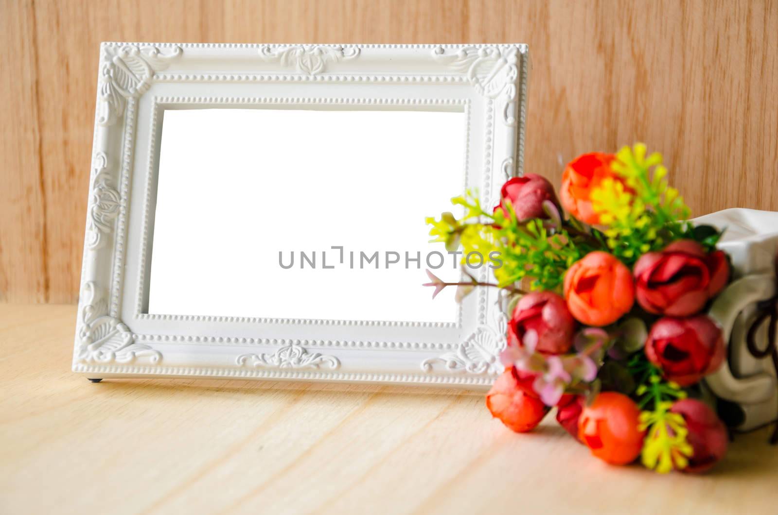 Flowers vase and vintage white picture frame on wooden desktop. by Gamjai