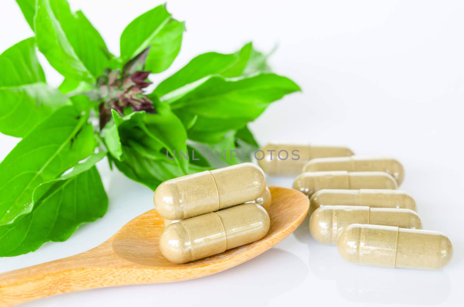 Herb capsule medicine in wooden spoon and green leaf on white background.