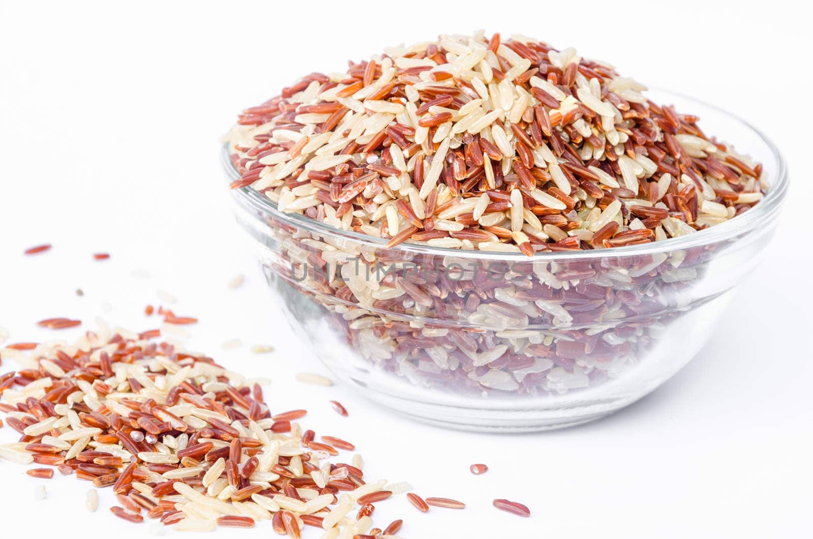 Raw brown rice in glass bowl on white background.