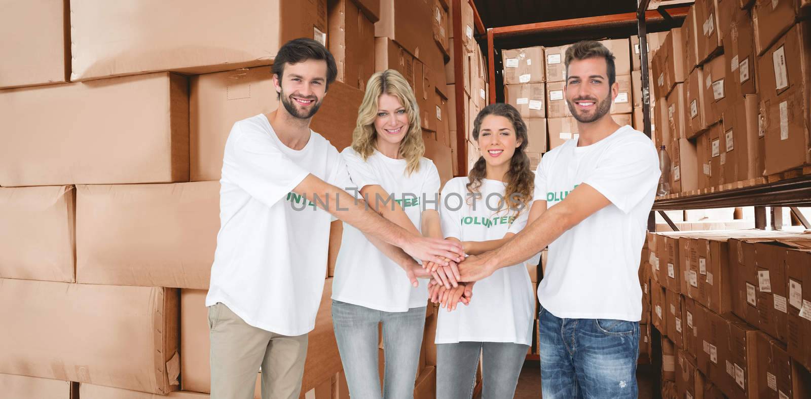 Group portrait of happy volunteers with hands together against shelves with boxes in warehouse