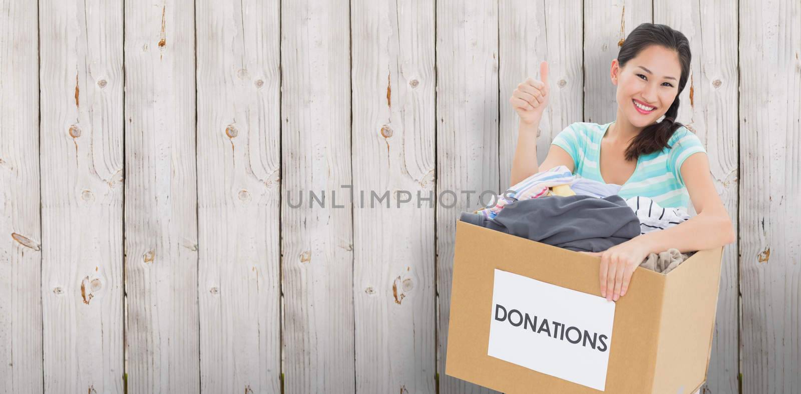 Woman with clothes donation gesturing thumbs up against wooden background