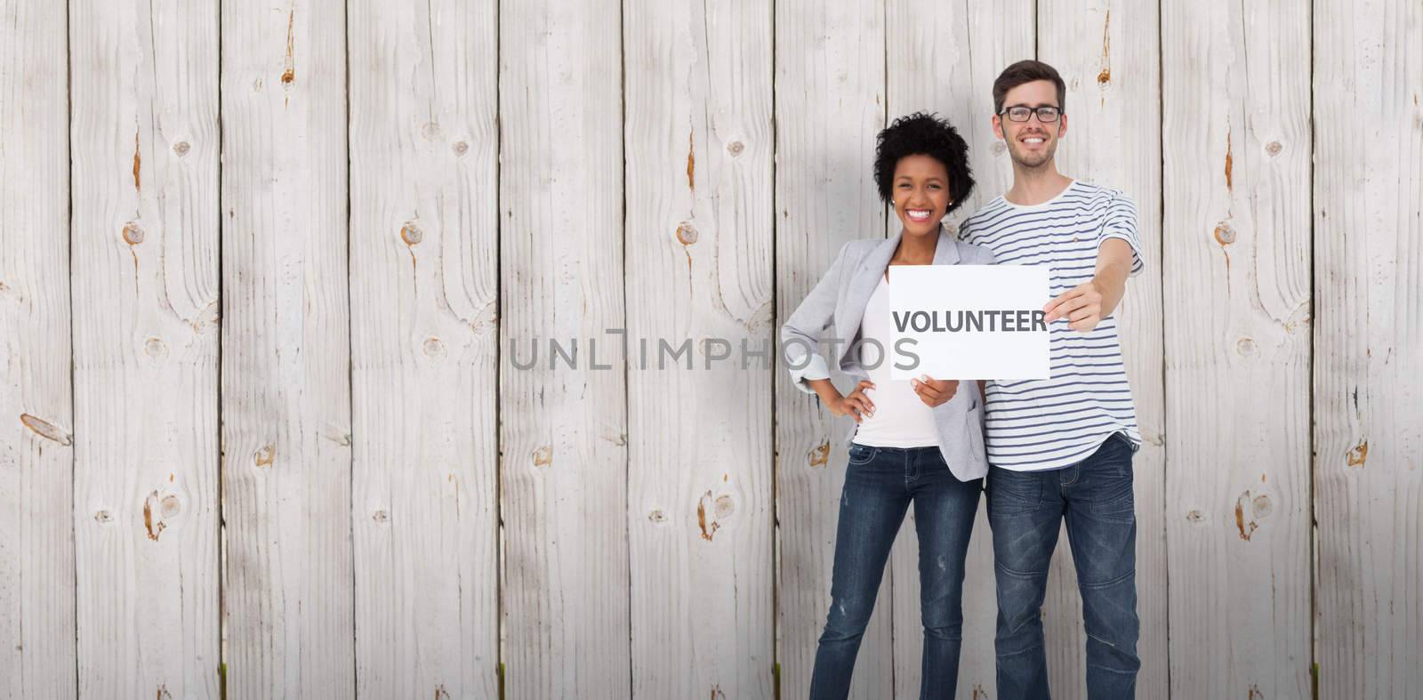 Portrait of a happy couple holding a volunteer note against wooden background