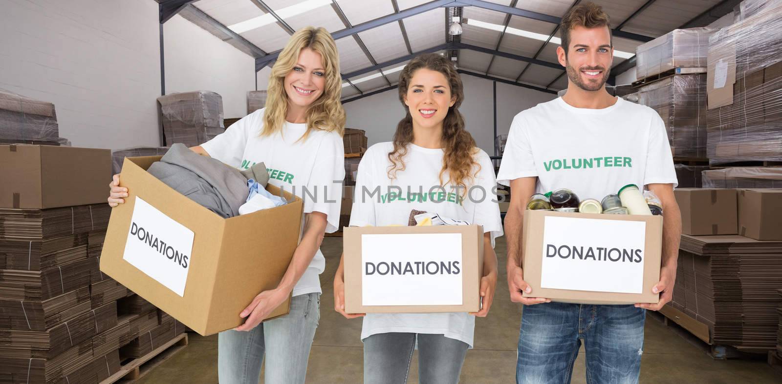 Portrait of three smiling young people with donation boxes against forklift in a large warehouse