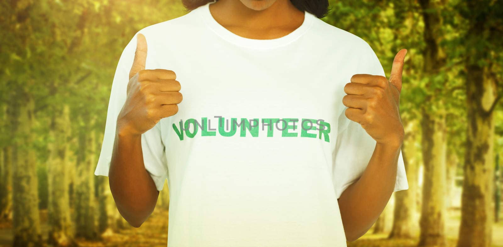 Woman wearing volunteer tshirt and giving thumbs up against walkway along lined trees in the park