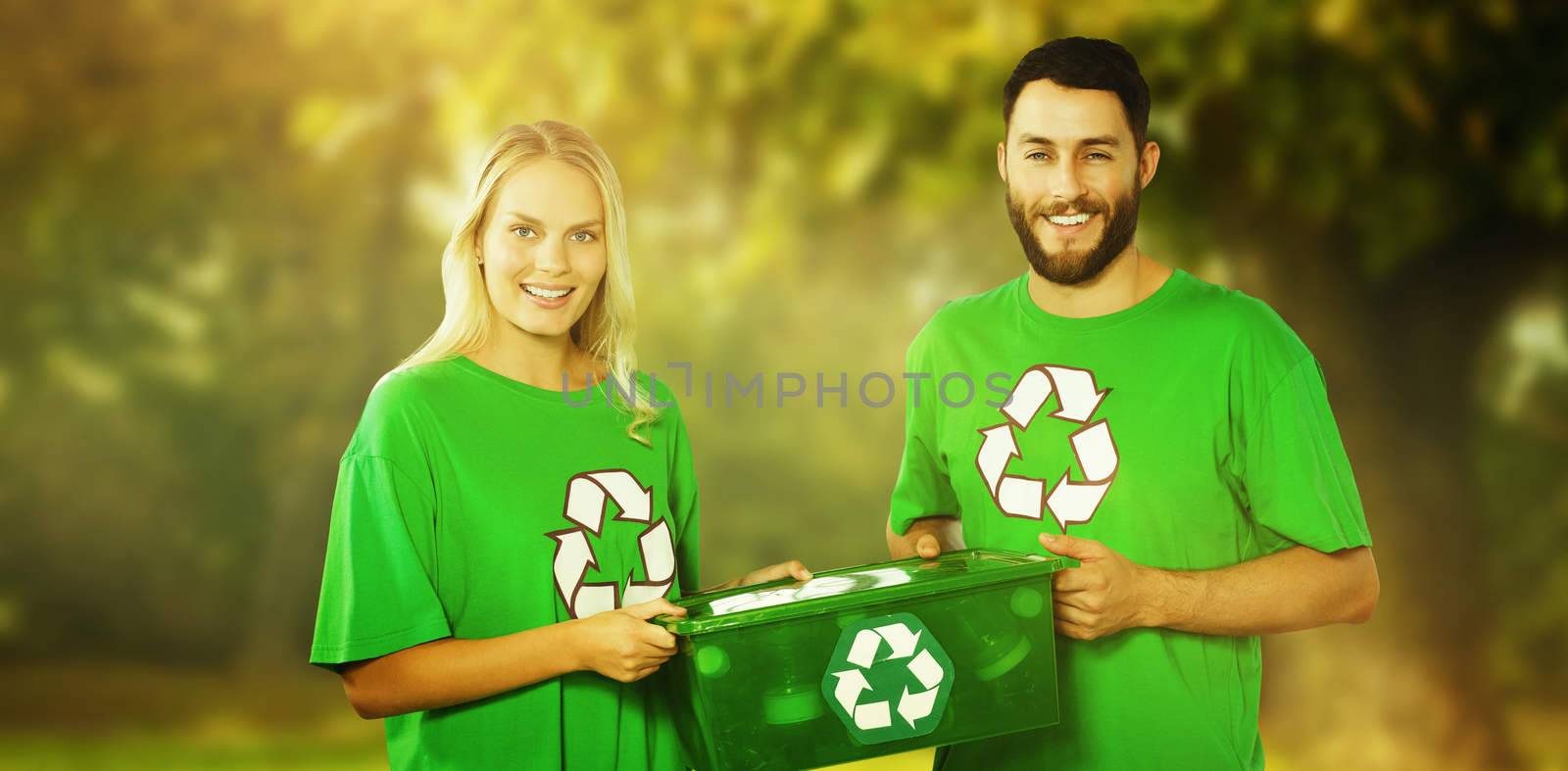 Portrait of smiling volunteers carrying recycling container  against trees and meadow in the park