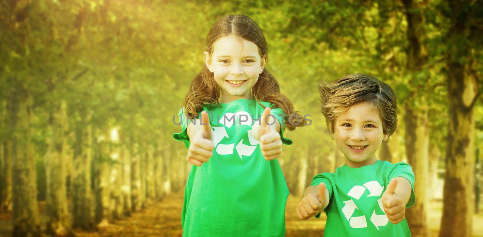 Happy siblings in green with thumbs up  against walkway along lined trees in the park