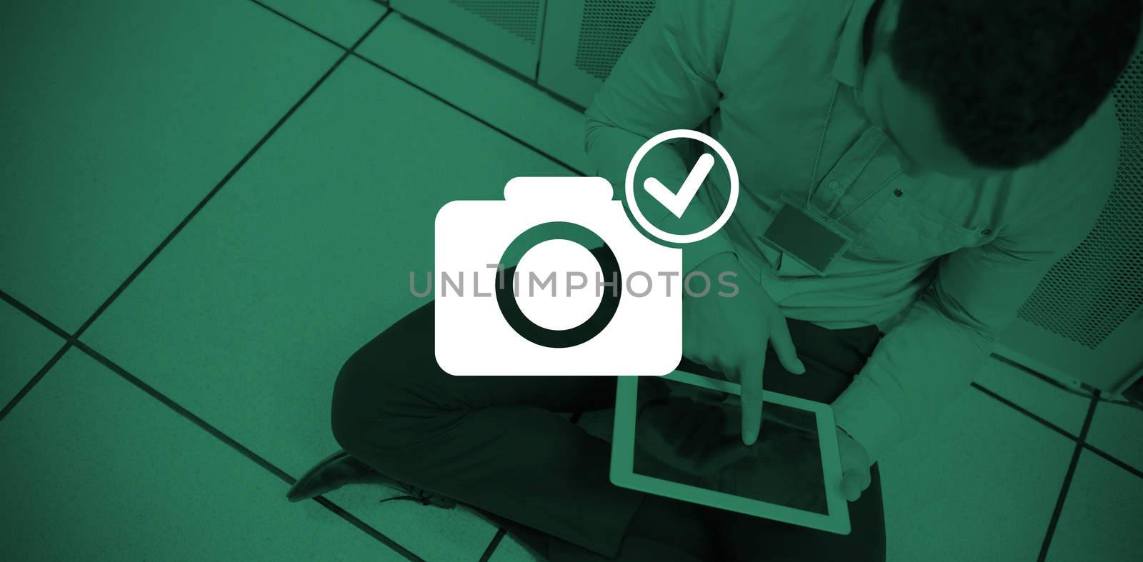 Digitally generated image of camera with tick symbol against businessman using digital tablet while sitting on office floor