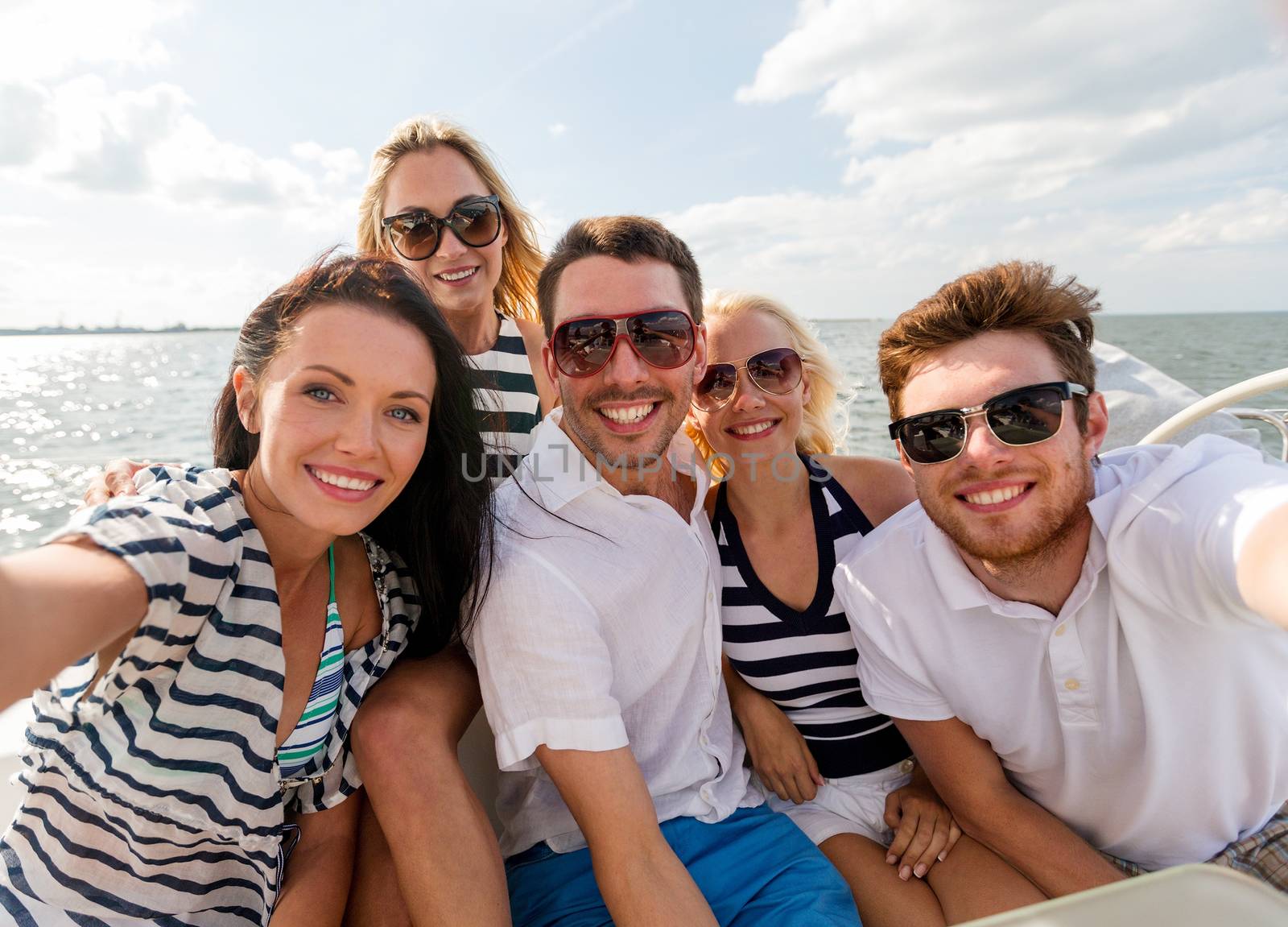 vacation, travel, sea, friendship and people concept - smiling friends sitting on yacht deck and making selfie