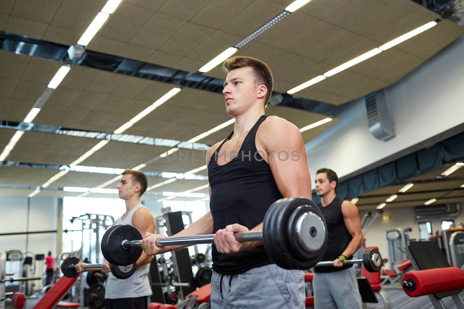 group of men flexing muscles with barbell in gym by dolgachov