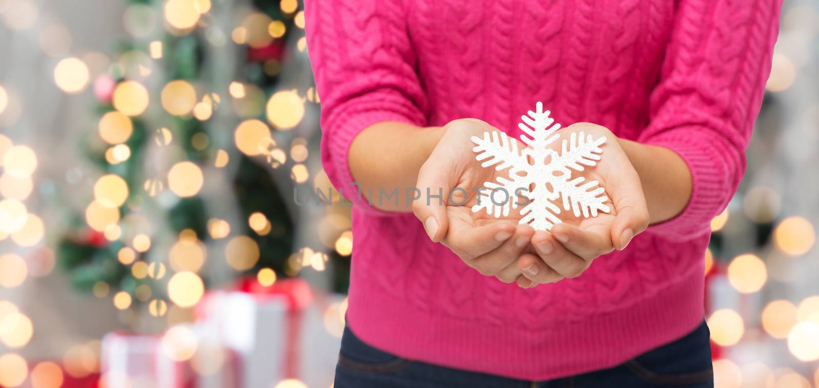 christmas, holidays and people concept - close up of woman in pink sweater holding snowflake decoration over tree lights background