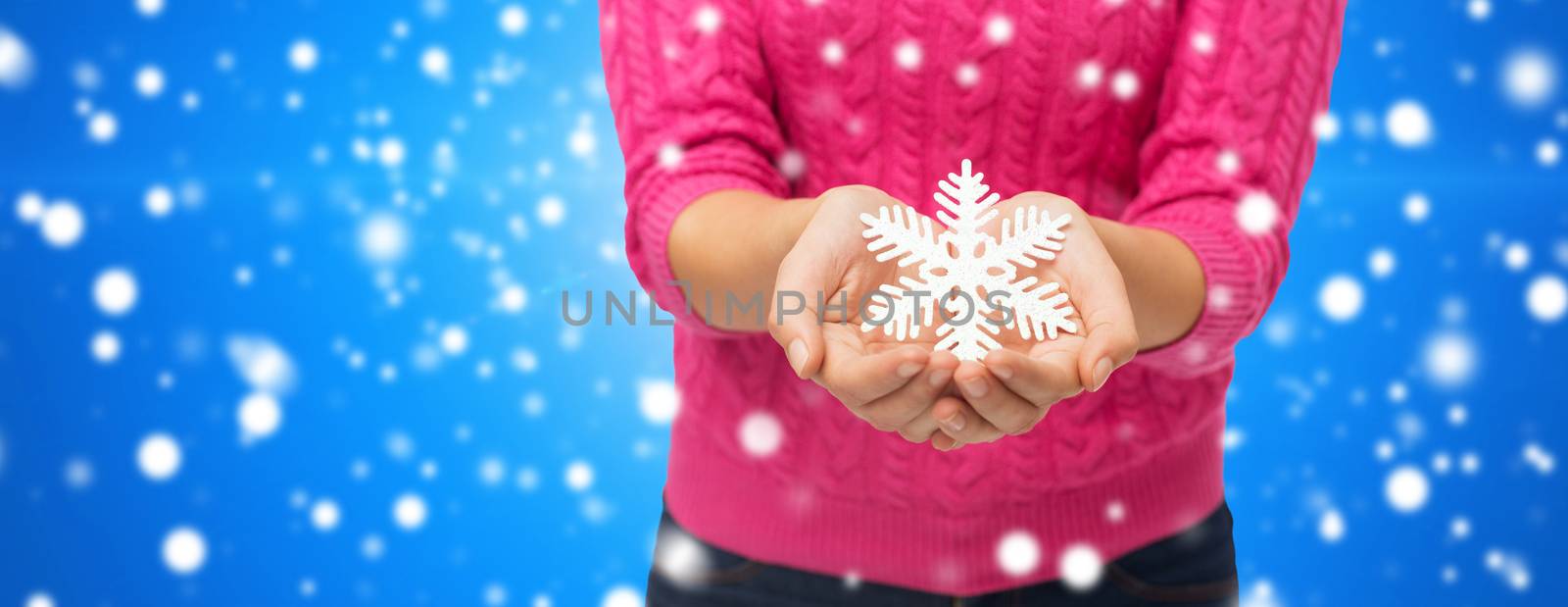 christmas, winter, holidays and people concept - close up of woman in pink sweater holding snowflake decoration over blue snowy background