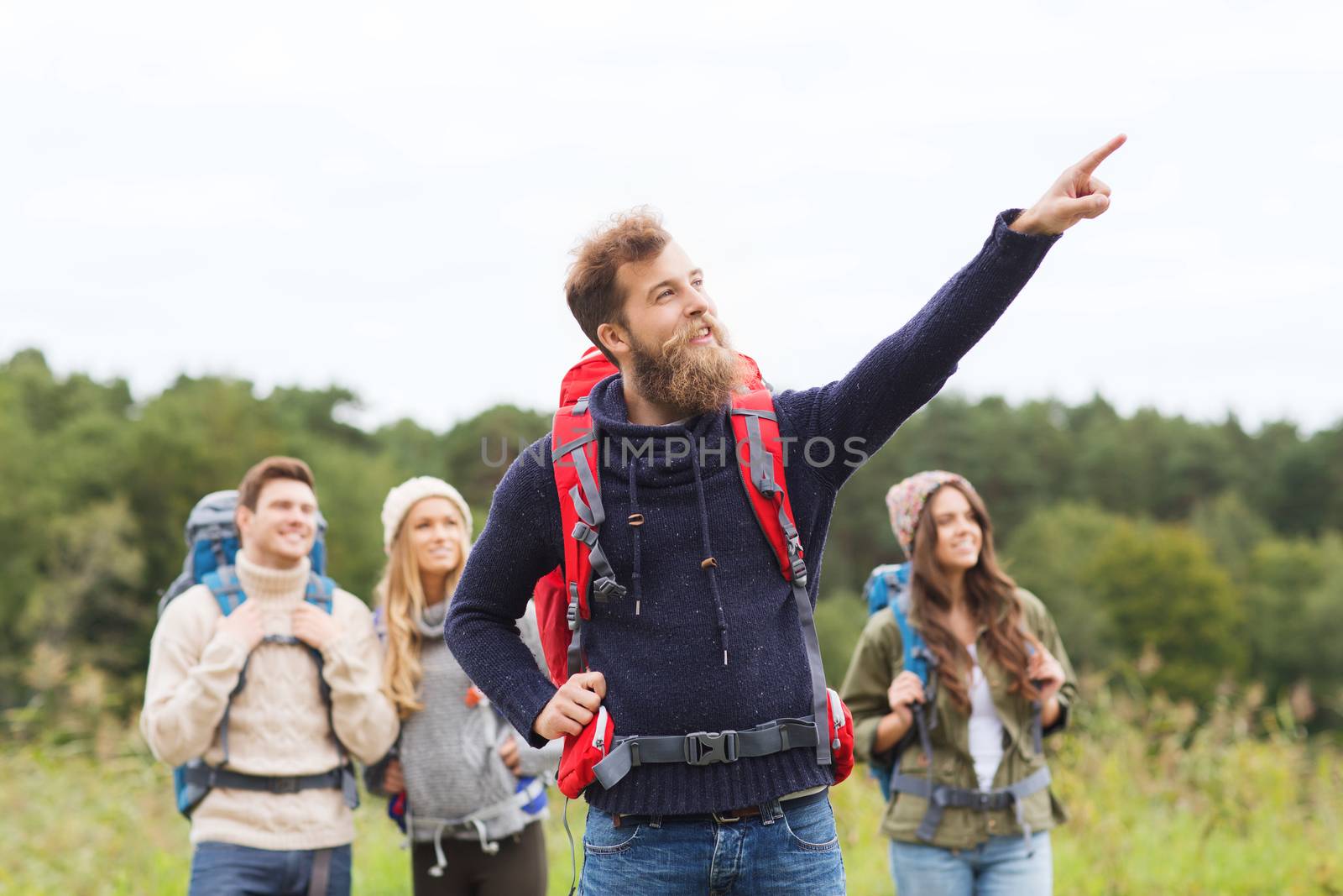 adventure, travel, tourism, hike and people concept - group of smiling friends with backpacks pointing finger outdoors