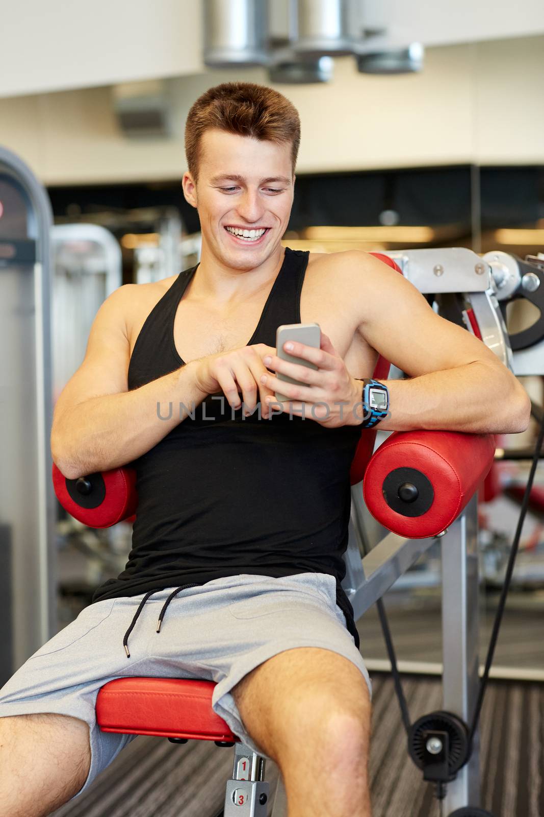 sport, bodybuilding, lifestyle, technology and people concept - smiling young man with smartphone in gym