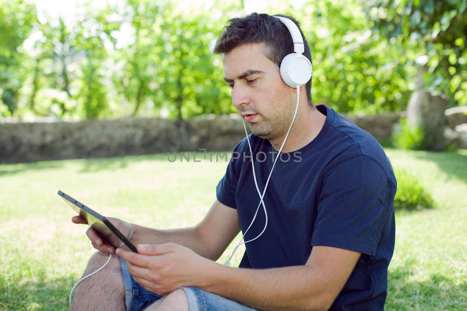 young man holding a tablet with headphones, outdoor