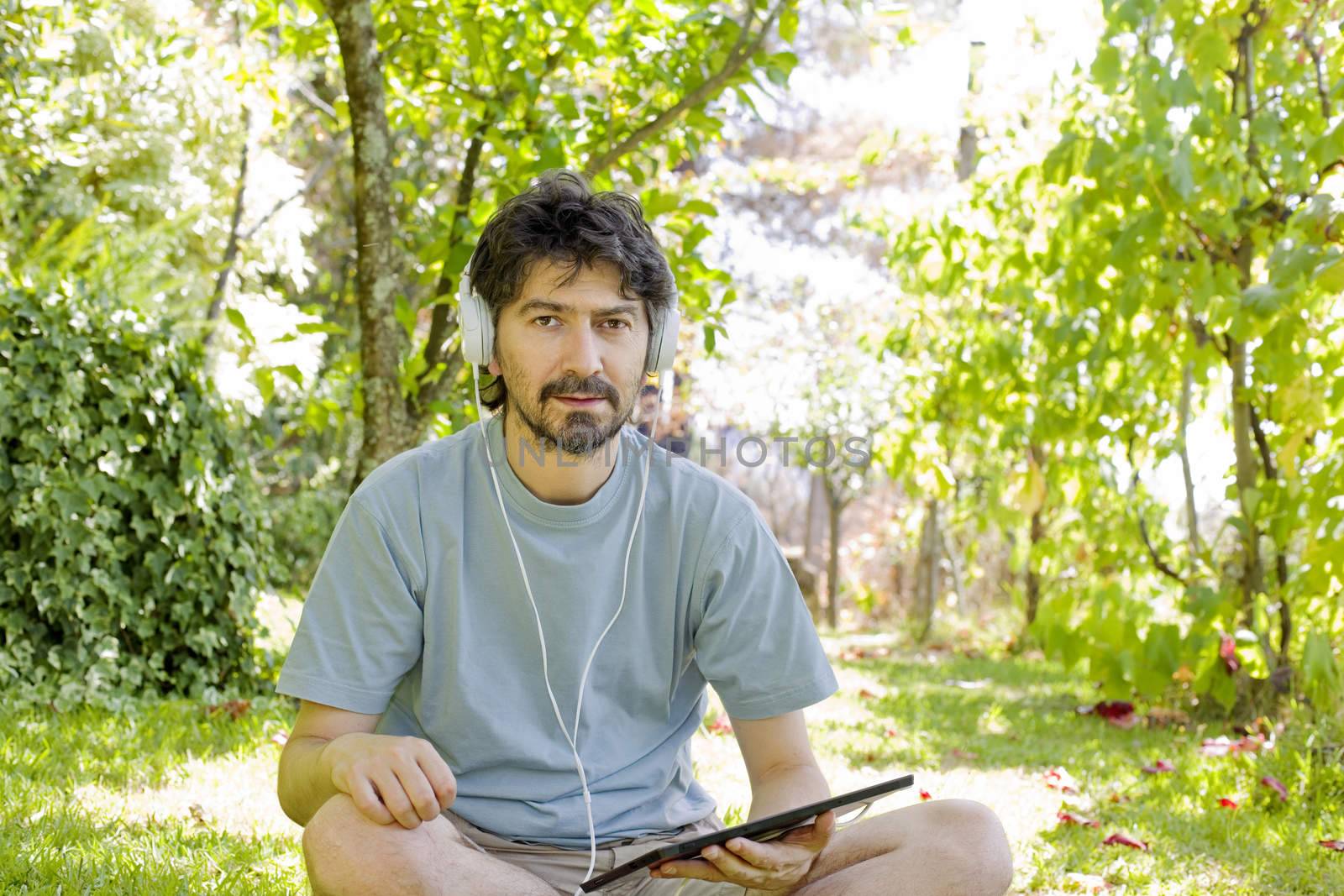 casual man holding a tablet with headphones, outdoor