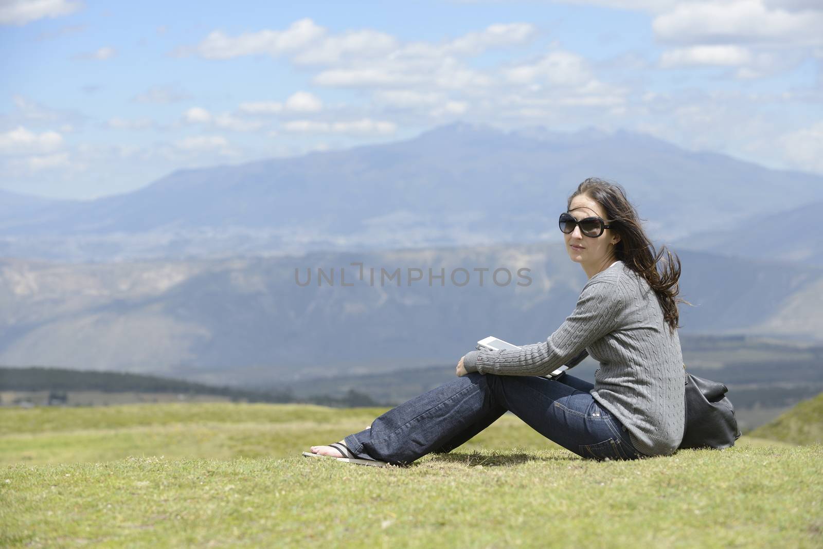 Woman in sunglasses is sitting on the grass in the mountains of Andes.