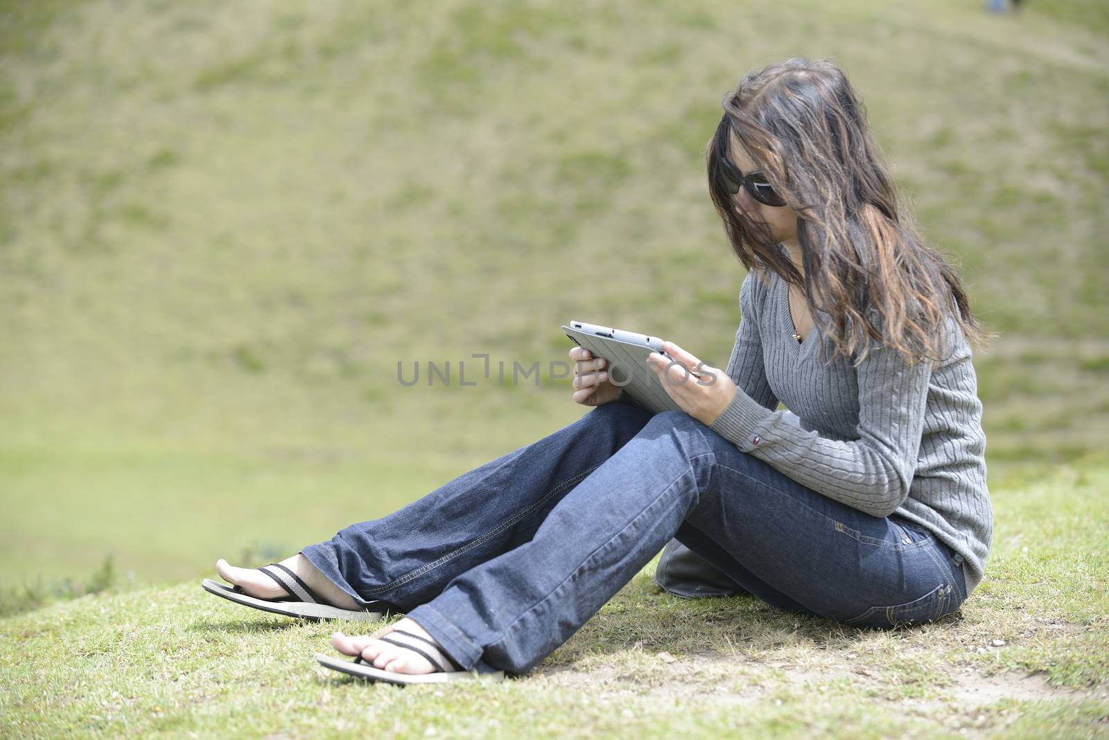 Woman in sunglasses is sitting on the grass and reading. by kertis