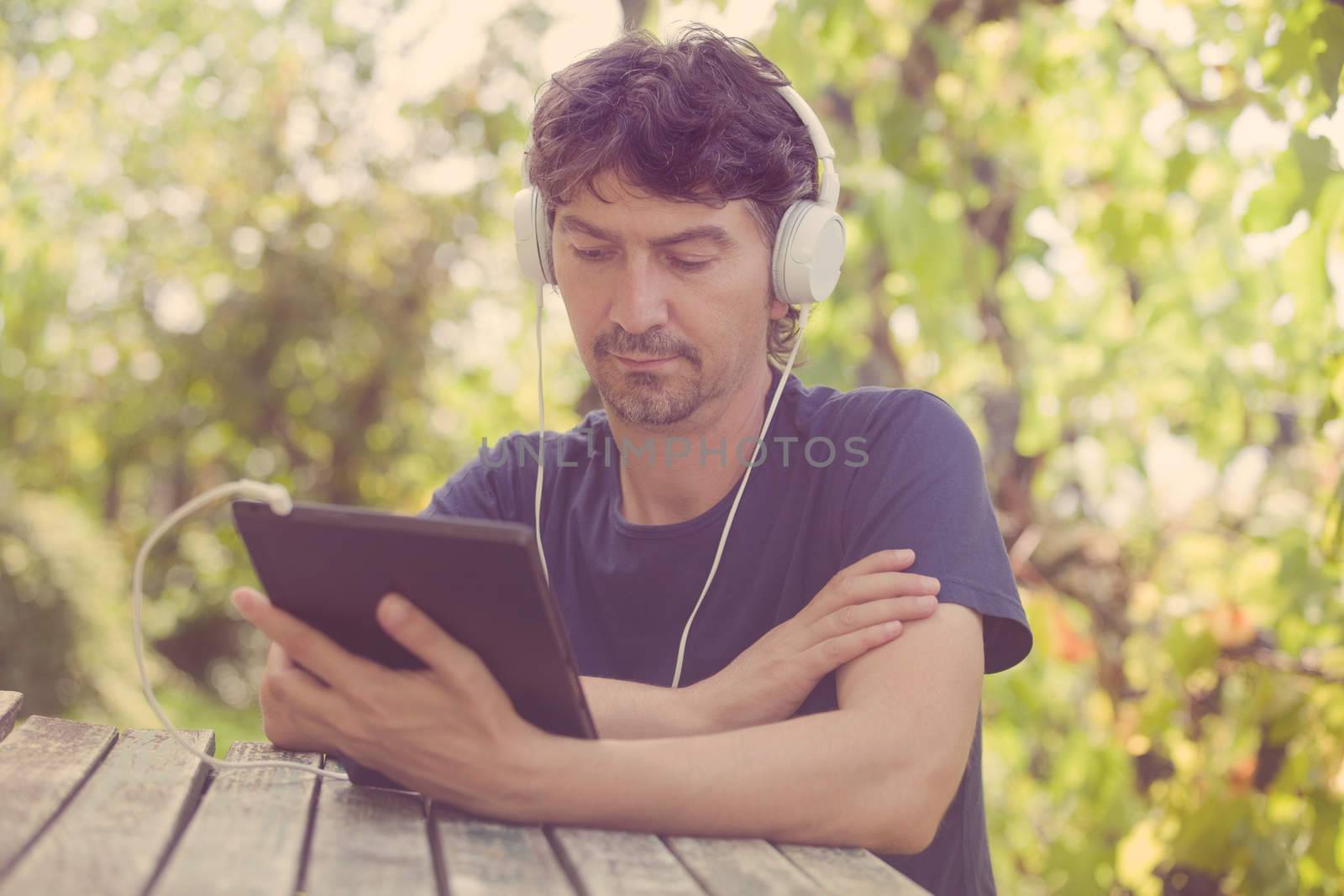 young man working with a tablet pc with headphones, outdoor, filtered image