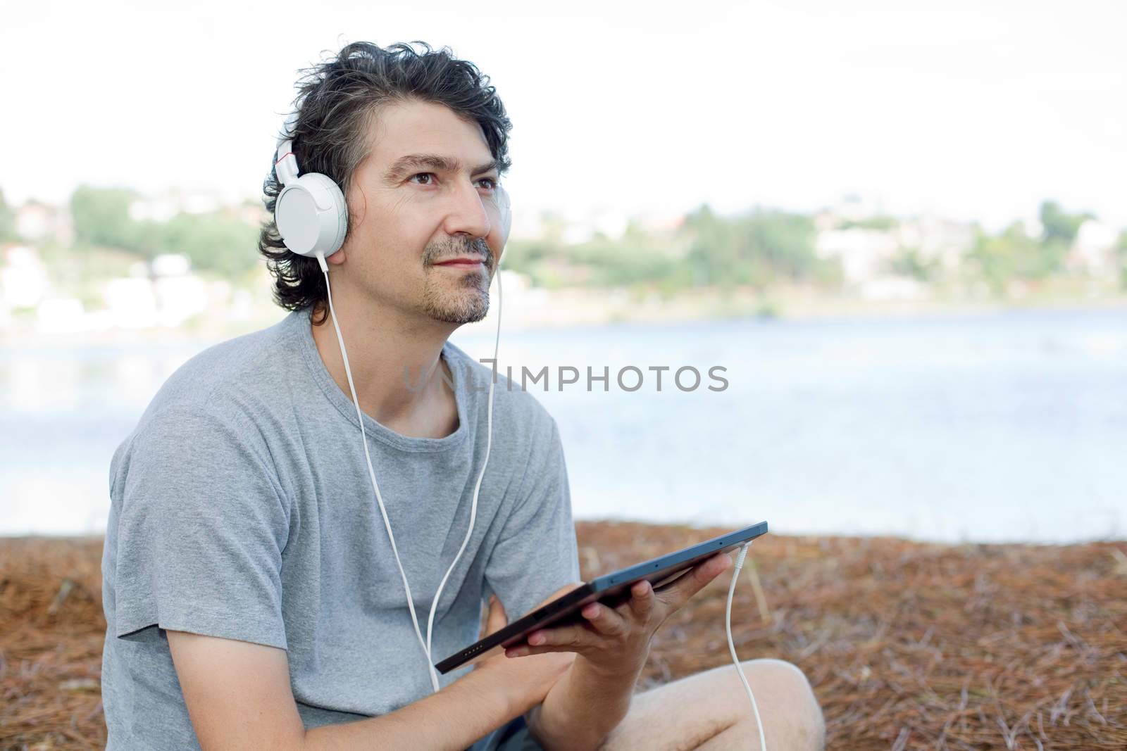 young man holding a tablet with headphones, at the beach