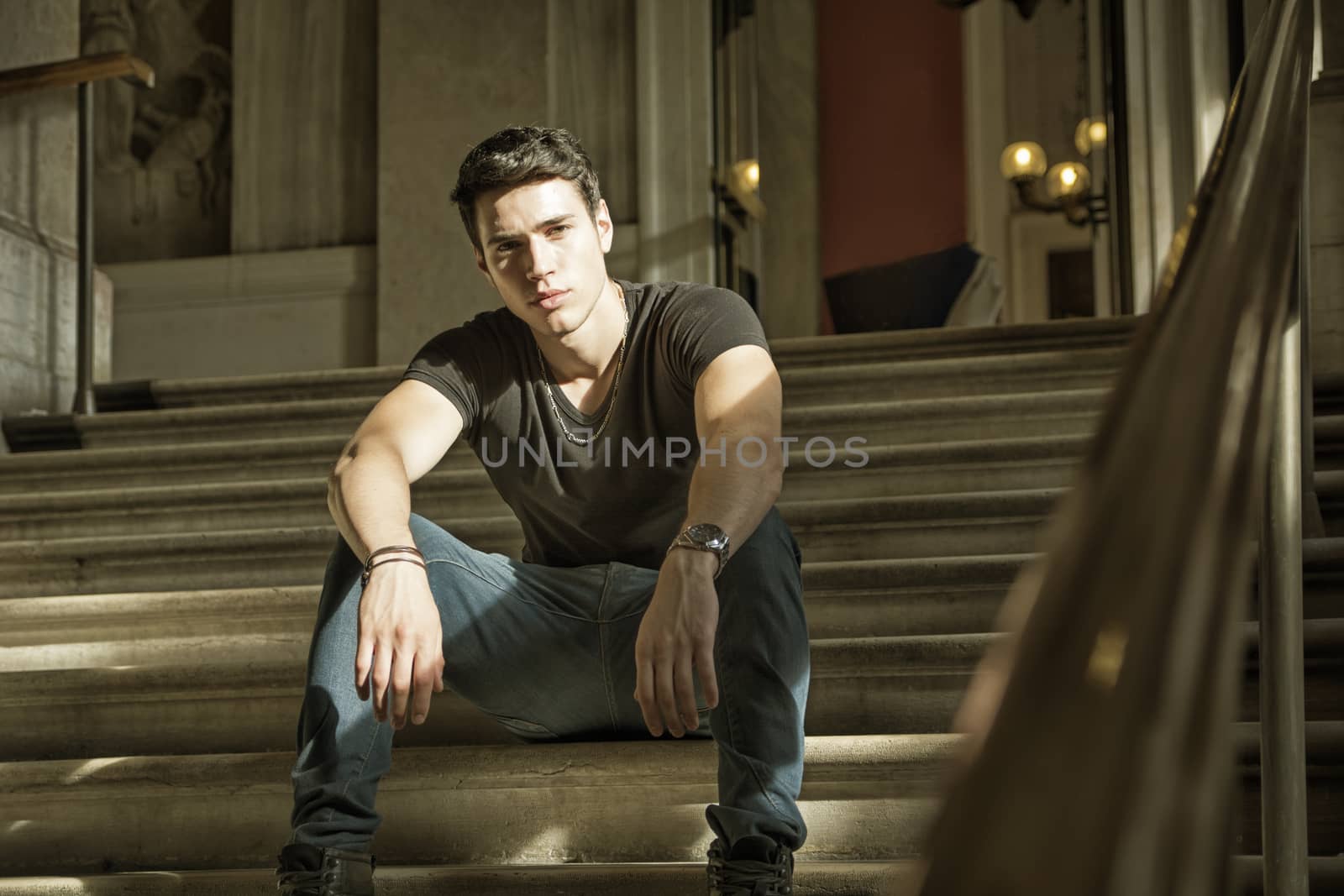 Young Handsome Man Sitting on Stairs Inside an Architectural Elegant Old Building While Looking at Camera