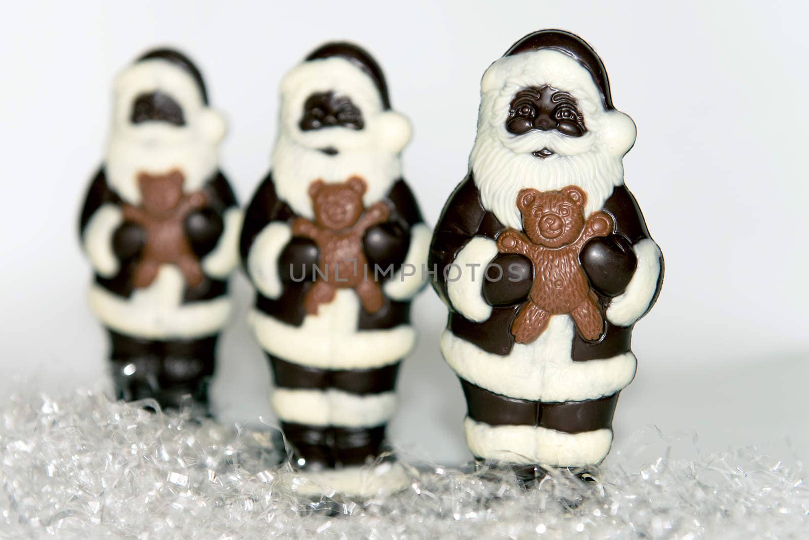 Close-up of a trio of chocolate santas on 'snow' with a whote background.