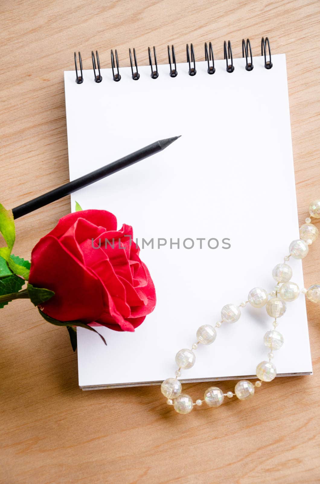 Red rose and black pencil with blank dairy on wooden background. For creative your message text here.