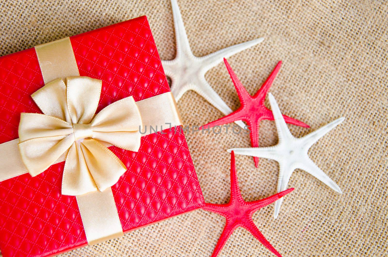 red gift box with gold ribbon and star fish on sack background