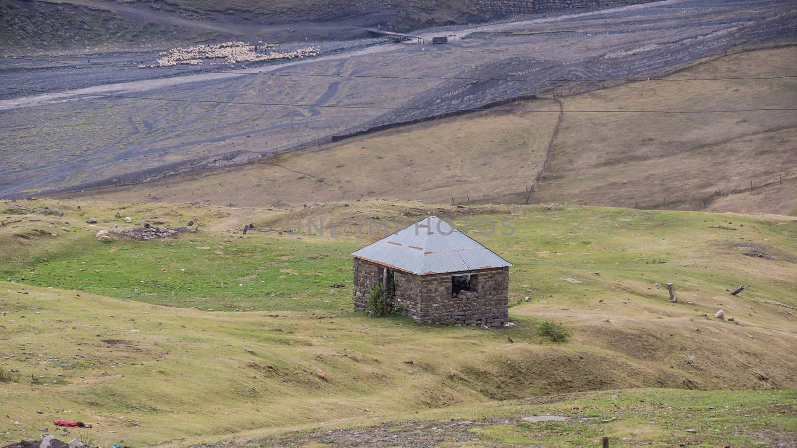 The shepherd's hut on the background of the river and a flock of sheeps in the distance in Great Caucasus Mountains, Azerbaijan.