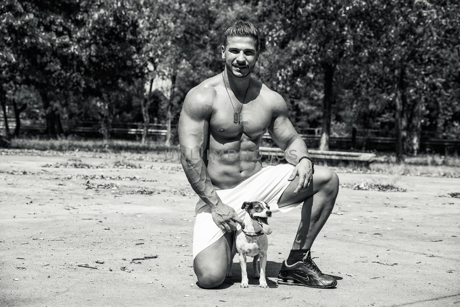 Full Body Shot of a Shirtless Athletic Young Man Kneeling with One Dog, Looking at Camera