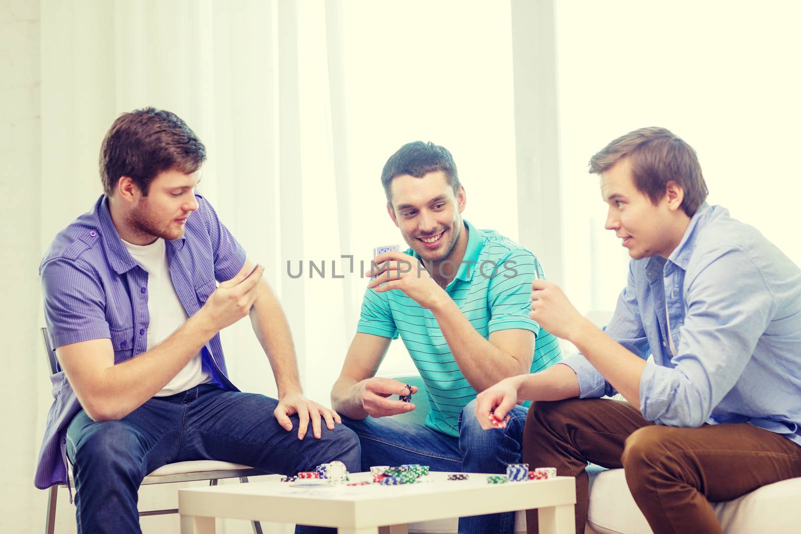 happy three male friends playing poker at home by dolgachov