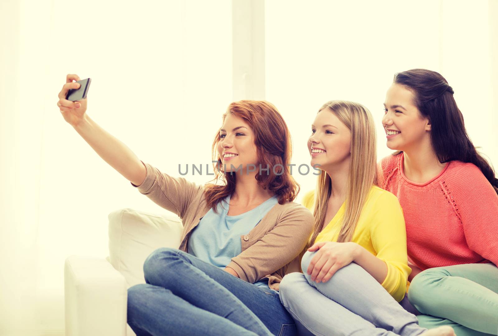 friendship, technology and internet concept - three smiling teenage girls taking selfie with smartphone camera at home