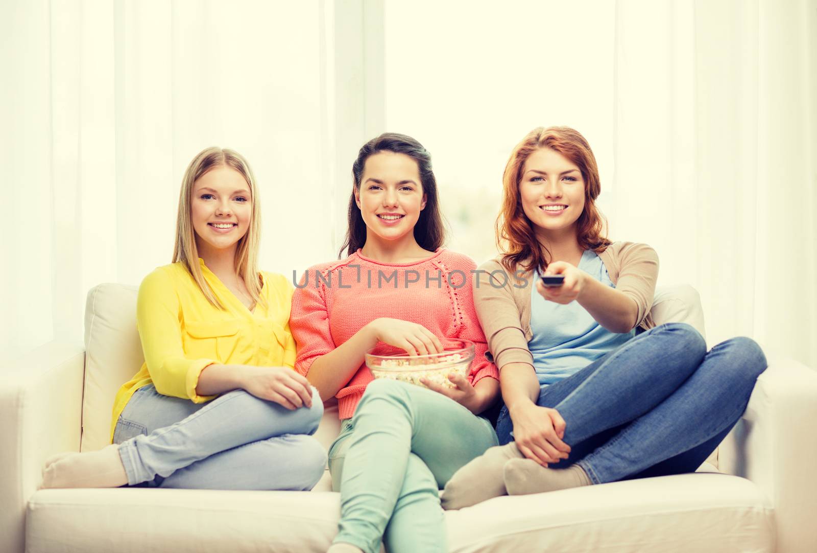 home, technology and friendship concept - three smiling teenage girl watching tv at home and eating popcorn