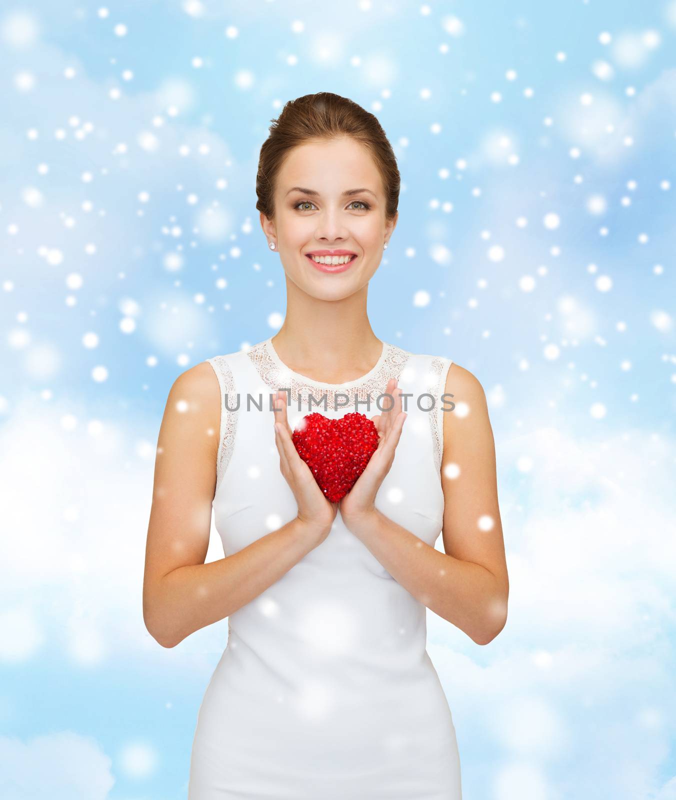 happiness, health, charity and love concept - smiling woman in white dress with red heart over blue cloudy sky and snow background