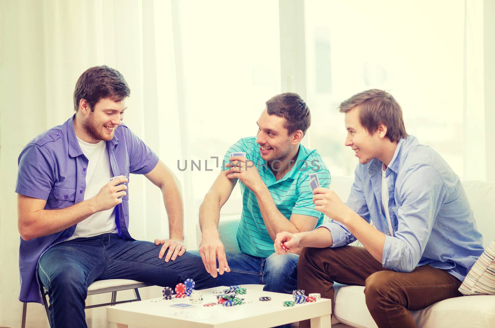 happy three male friends playing poker at home by dolgachov