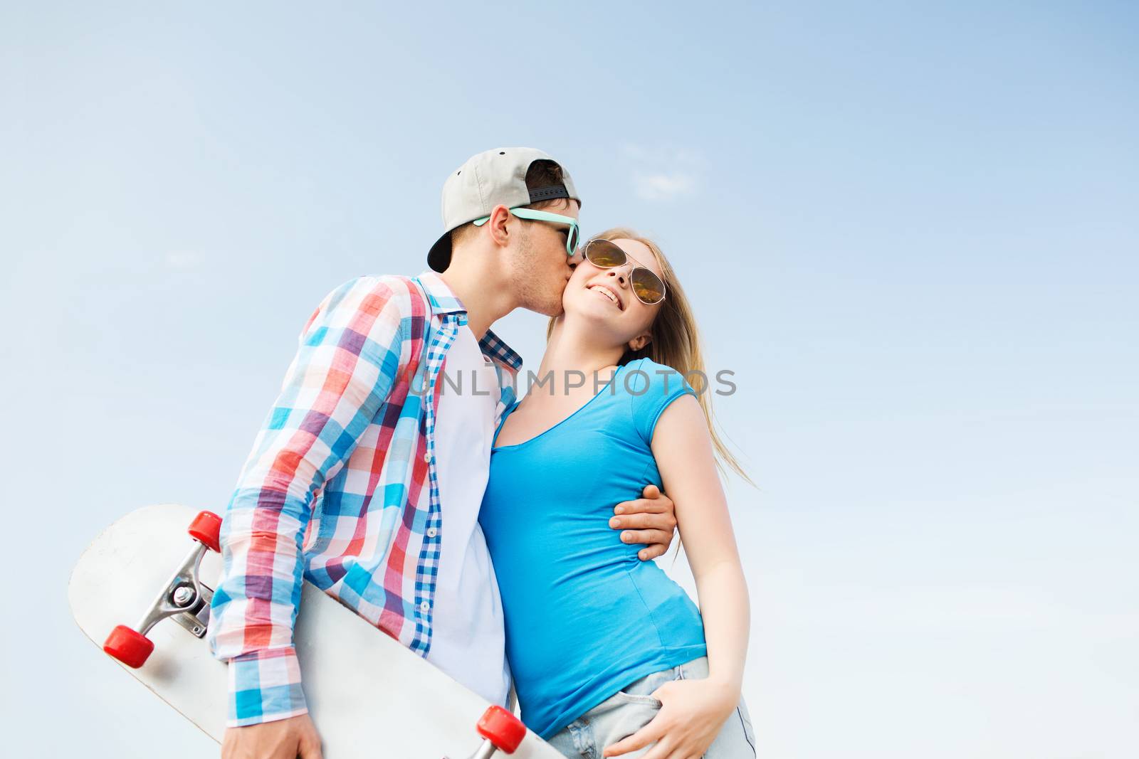 holidays, vacation, love and friendship concept - smiling couple with skateboard kissing outdoors
