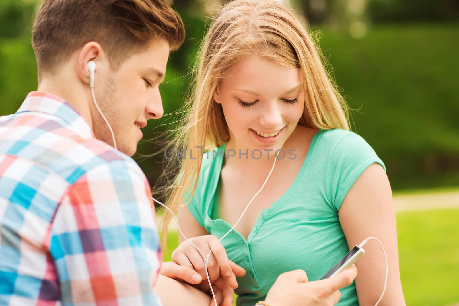 summer, vacation, holidays, technology and friendship concept - smiling couple with smartphone and earphones sitting in park