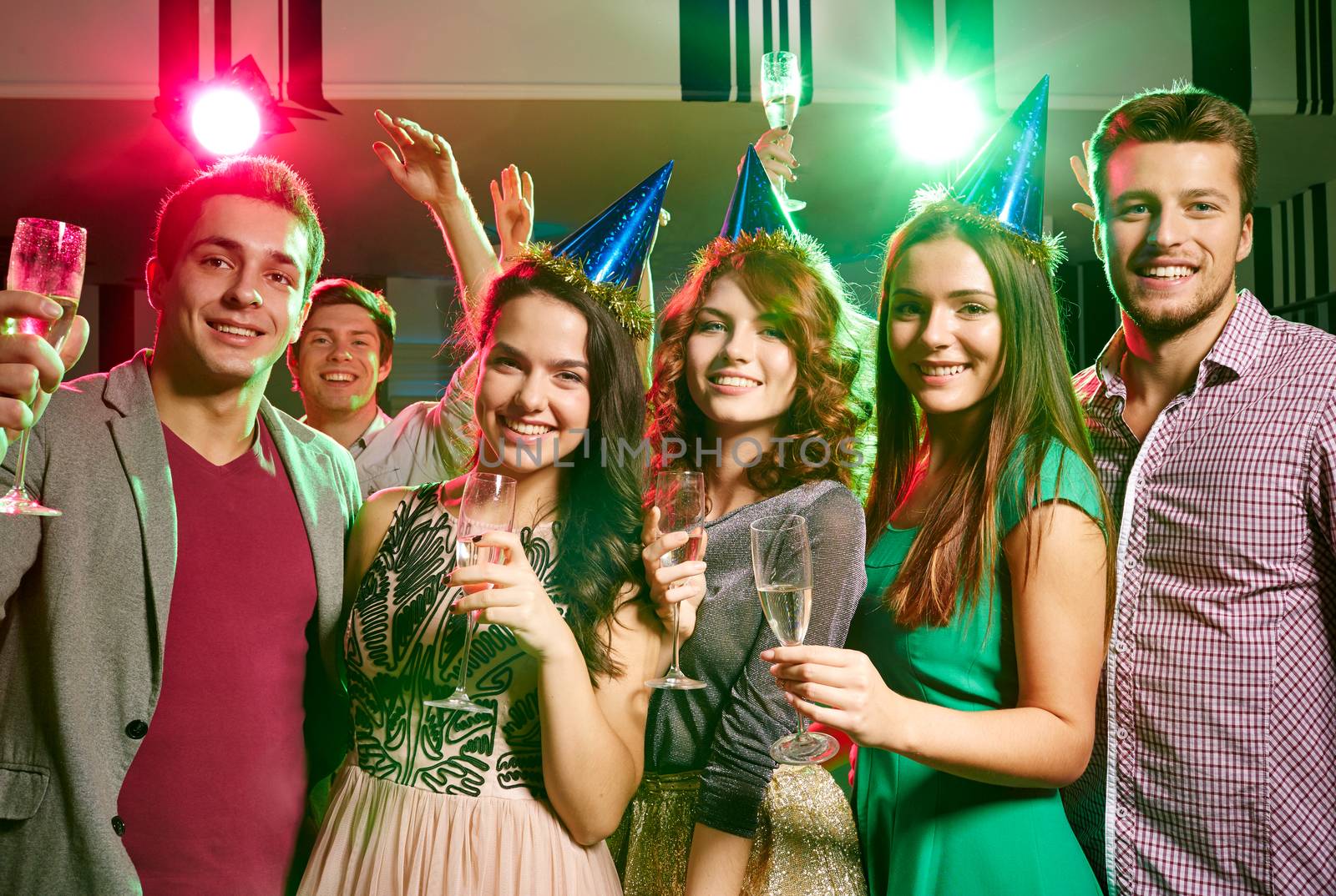 party, holidays, celebration, nightlife and people concept - smiling friends in party caps with glasses of champagne in club