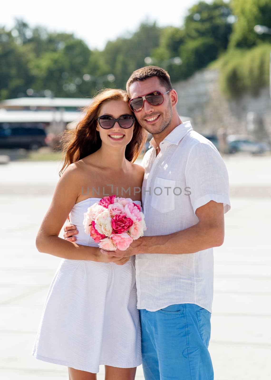 love, wedding, summer, dating and people concept - smiling couple wearing sunglasses with bunch of flowers hugging in city