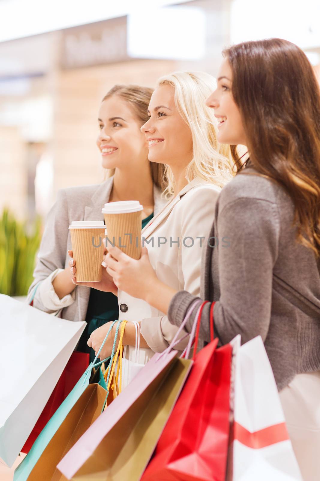 sale, consumerism and people concept - happy young women with shopping bags and coffee paper cup in mall