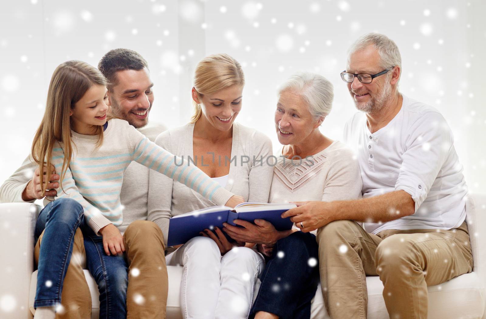 family, happiness, generation and people concept - happy family with book or photo album sitting on couch at home